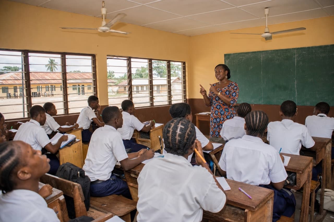 Modern Nigerian classroom with teacher, students in uniform, and local school building